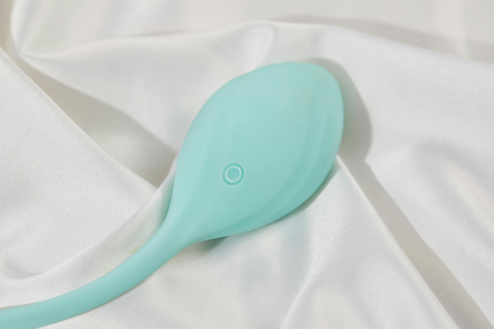 A teal silicone vibrator resting on white silk fabric, representing modern intimacy tools for reconnecting couples