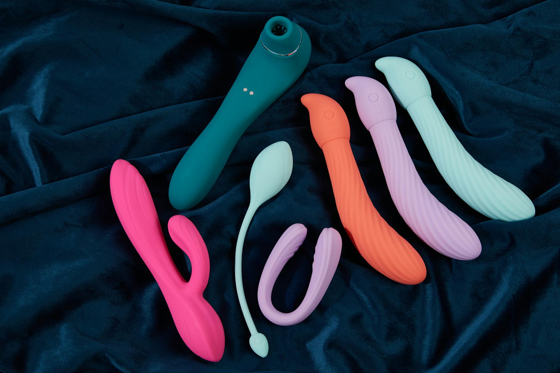Close-up of a hand holding an orange vibrator against a minimalistic purple backdrop, showcasing modern sensuality