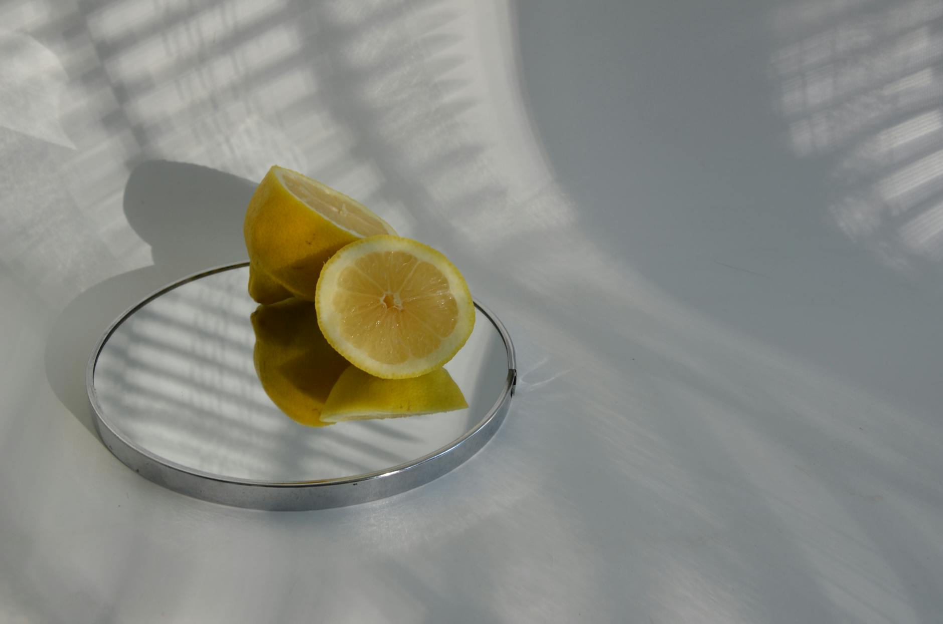 Limoni affettati su uno specchio che proietta ombre, mostrando una fotografia minimalista di alimenti