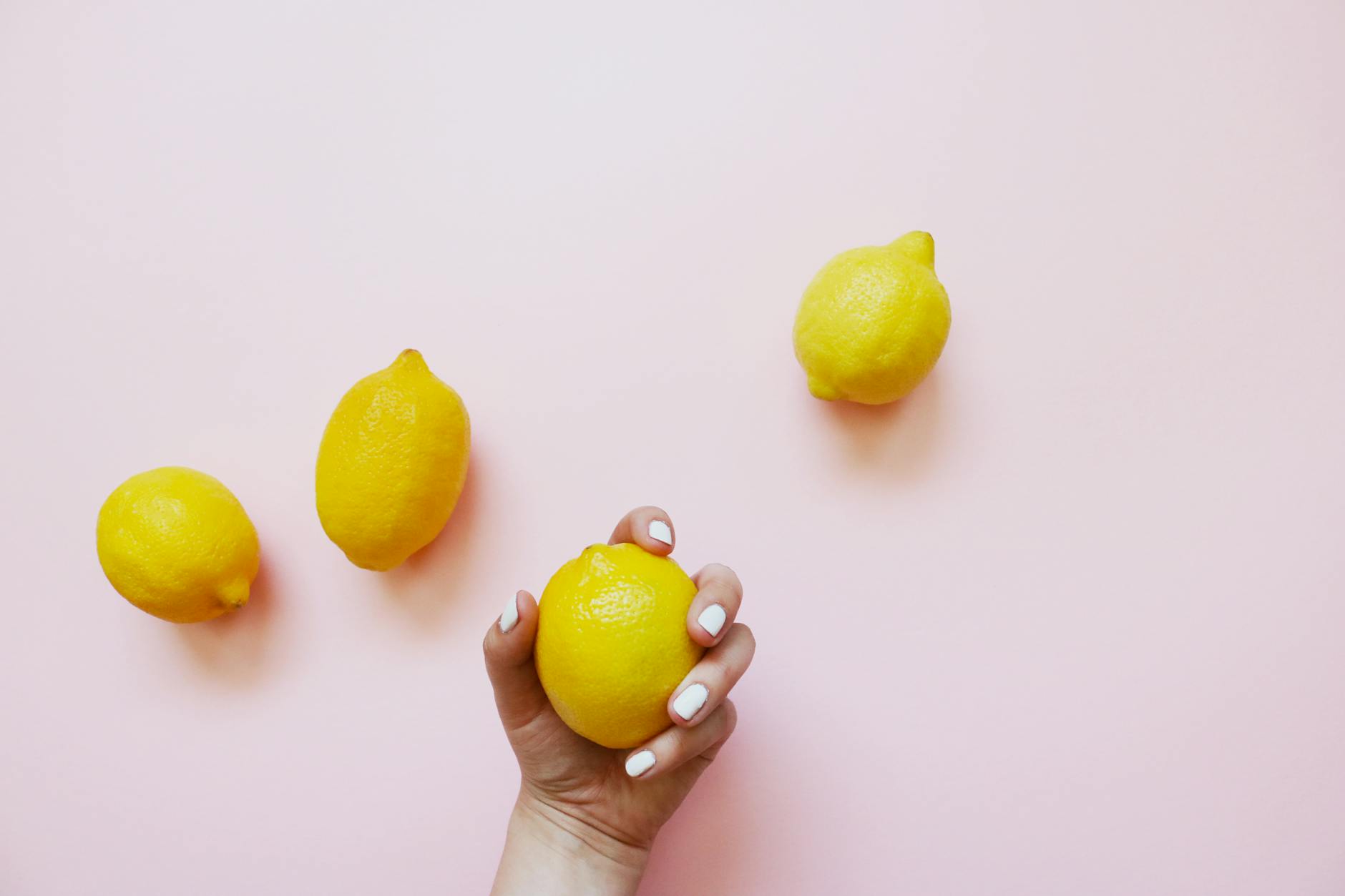 A hand holding a lemon on a soft pink background, symbolizing comfort and self-care for those with endometriosis