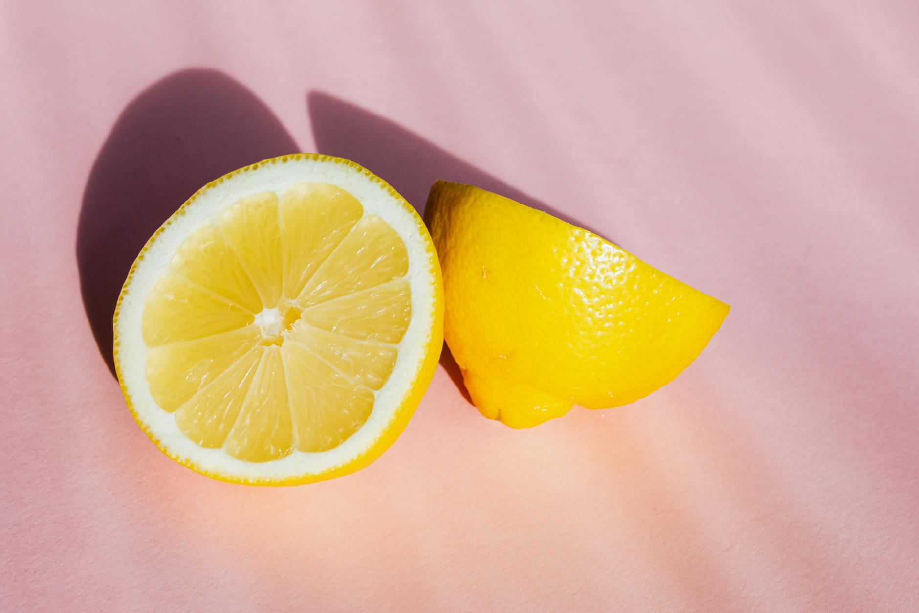 Fresh lemon halves on pink background in sunlight