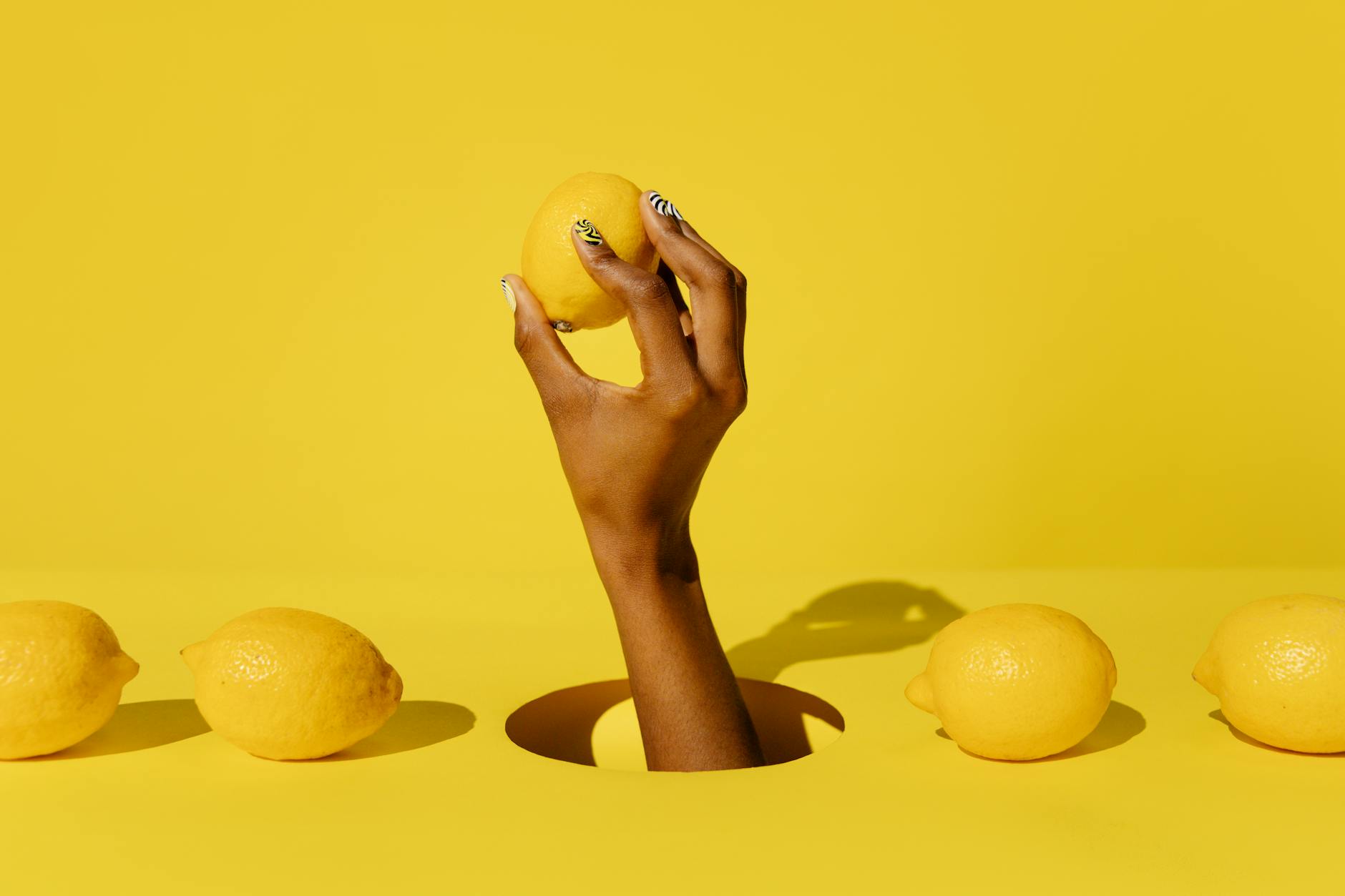 A creative composition featuring a hand holding a lemon against a vivid yellow background, conveying a fresh and citrusy vibe.