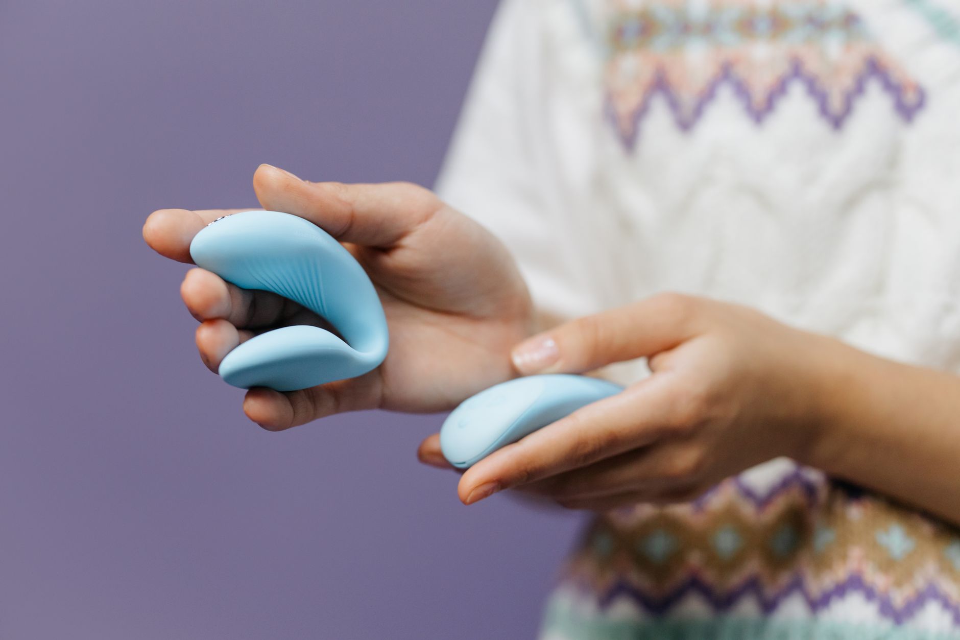 Hands holding a sleek blue vibrator against a purple background, representing intimate recovery tools.