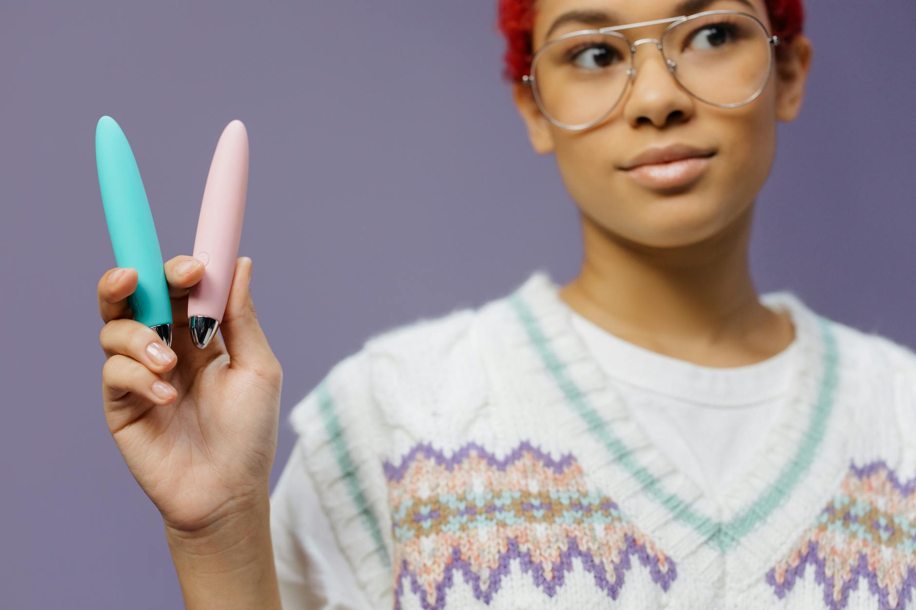 A person holding a colorful vibrator against a purple background, representing modern intimate wellness tools