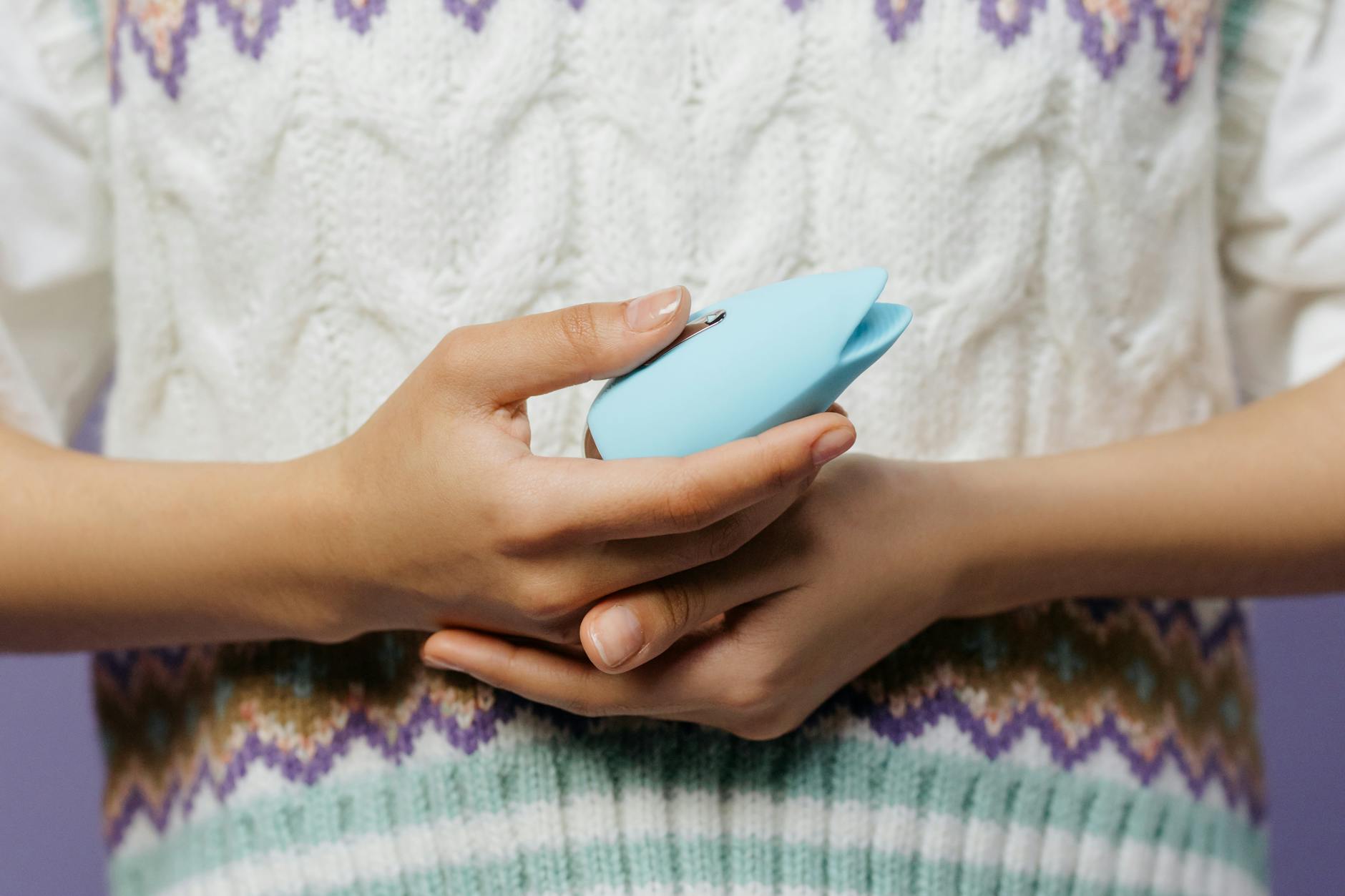 Hand holding a blue silicone clitoral vibrator against a purple background, showcasing intimate wellness for mature bodies